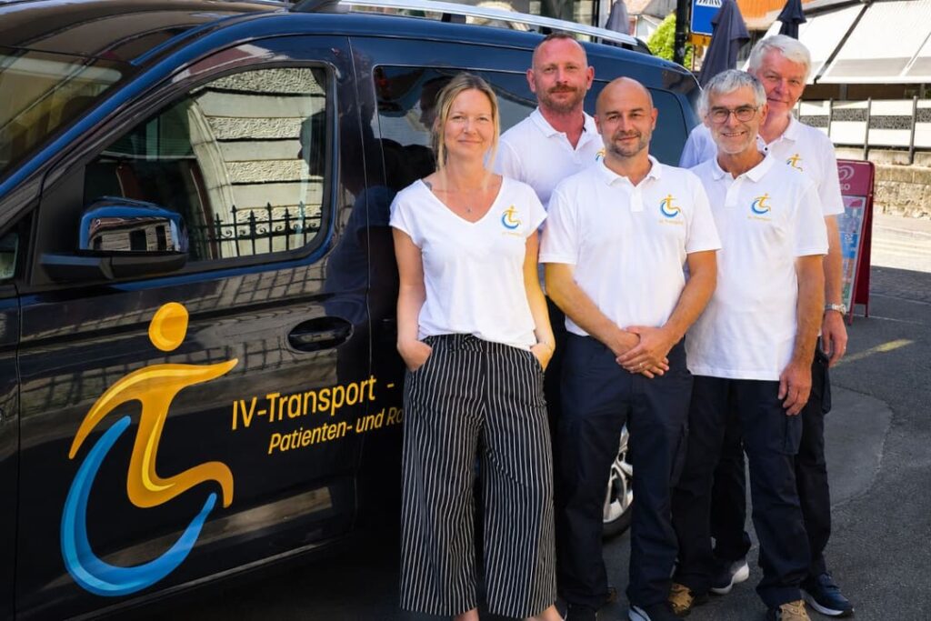 Team von IV Transport vor einem modernen Transportfahrzeug für Patienten- und Rollstuhltransporte